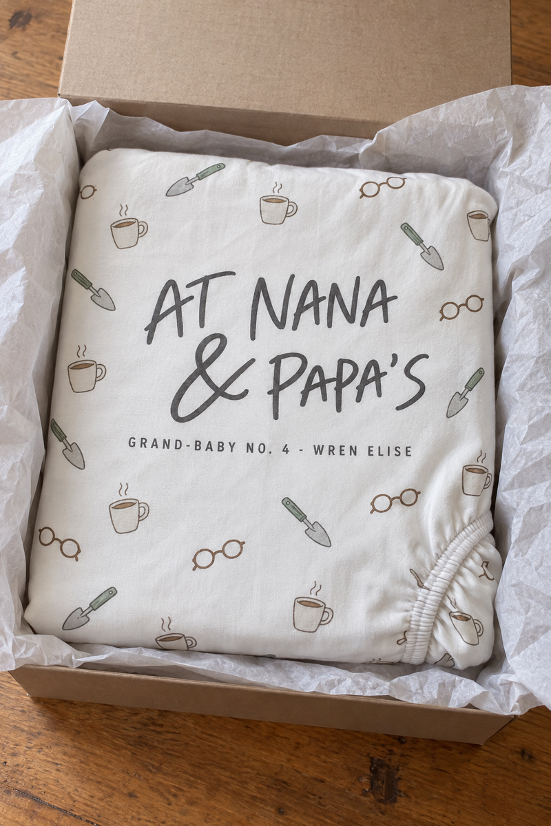 A folded custom fitted crib sheet with a printed nursery pattern beside a wrapped gift box