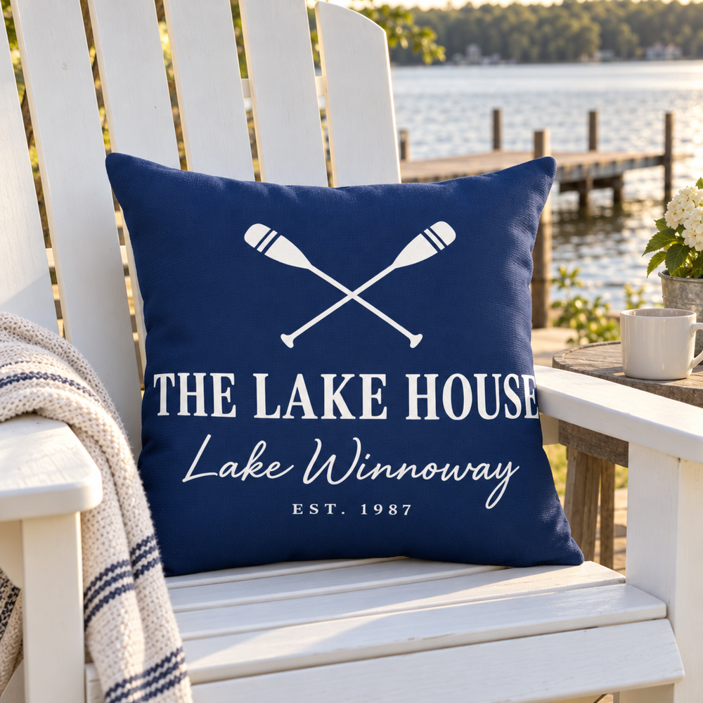 Navy custom outdoor pillow reading The Lake House on a white Adirondack chair on a lake deck
