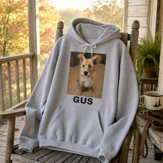 Sport grey custom hoodie printed with a candid terrier photo and the name Gus, draped over a porch rocking chair on a fall morning
