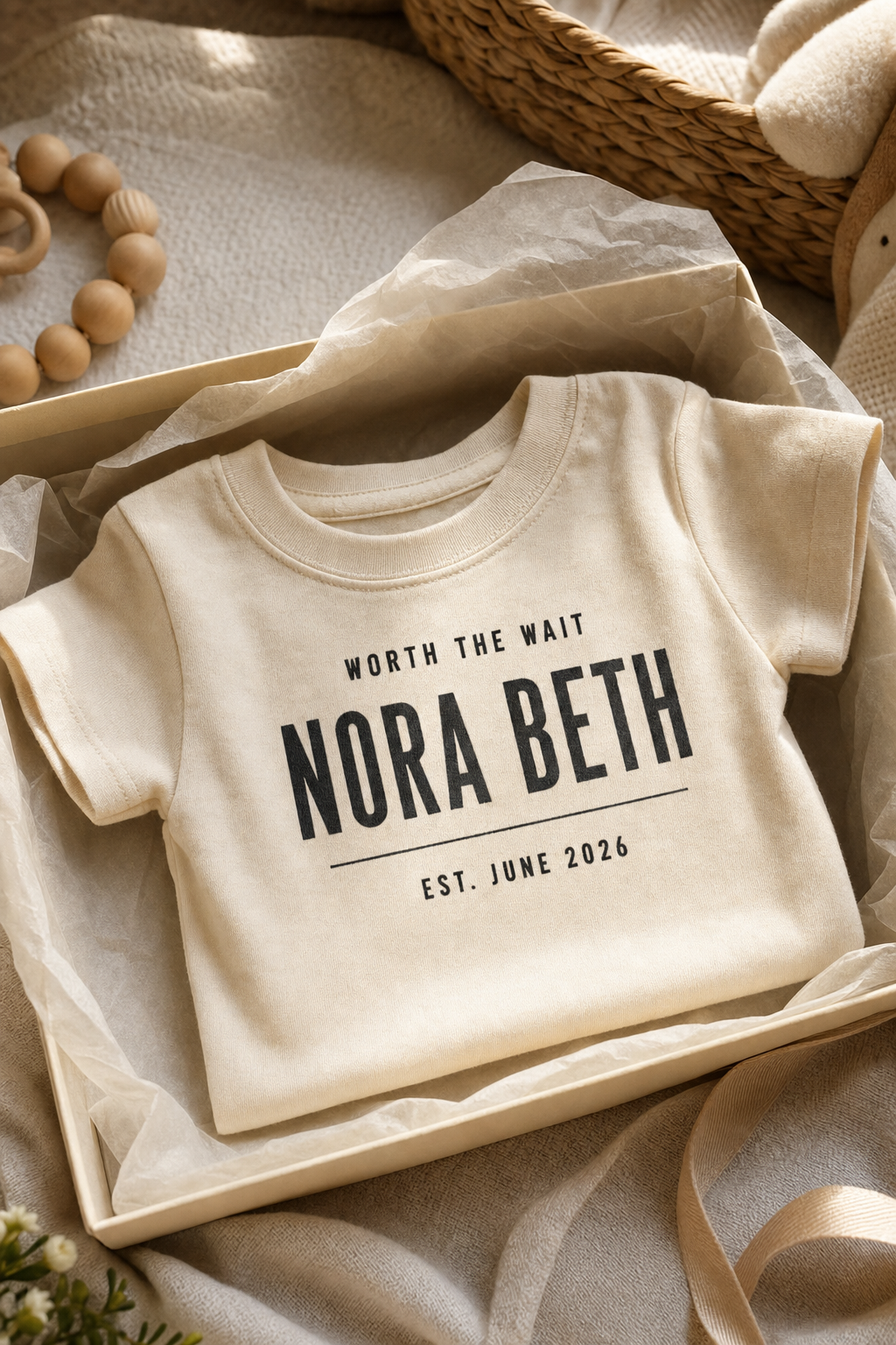 Cream infant tee printed with WORTH THE WAIT, NORA BETH, EST. JUNE 2026, folded in a gift box with tissue paper