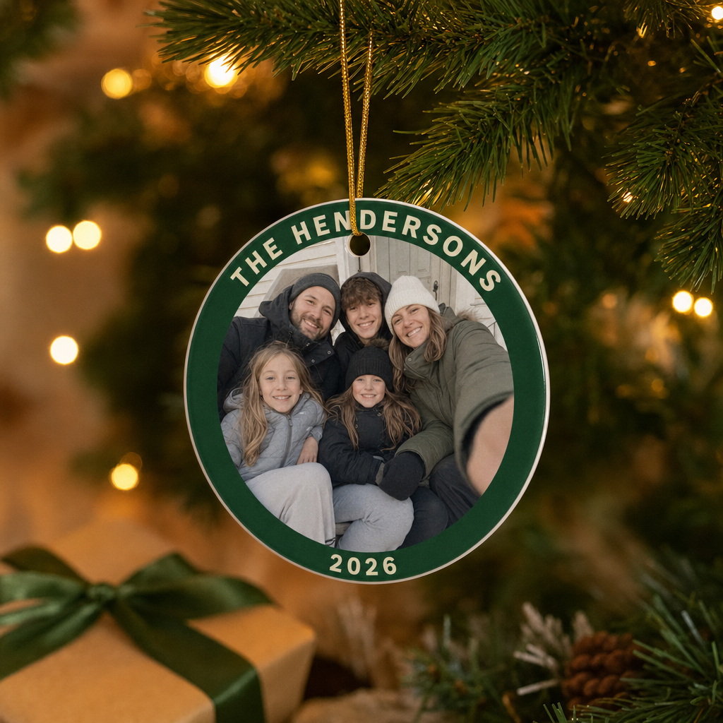 Personalized ceramic circle ornament with a family porch photo and the name The Hendersons 2026 hanging on a lit Christmas tree