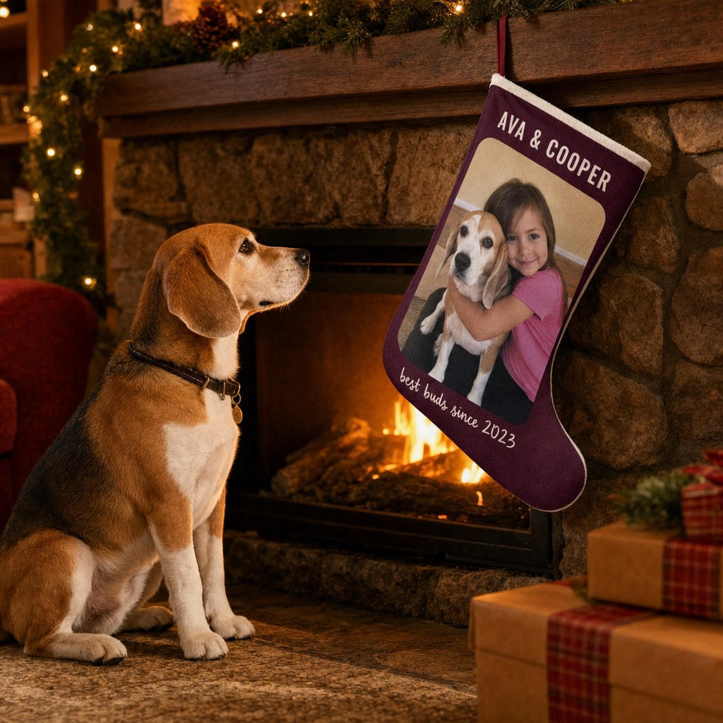 A beagle sitting by the fireplace next to a personalized stocking printed with a photo of a girl hugging that same beagle