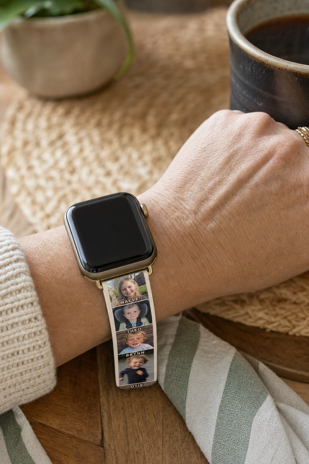 Custom Apple Watch band printed with a column of grandchildren's photos and their names, worn while holding a coffee mug