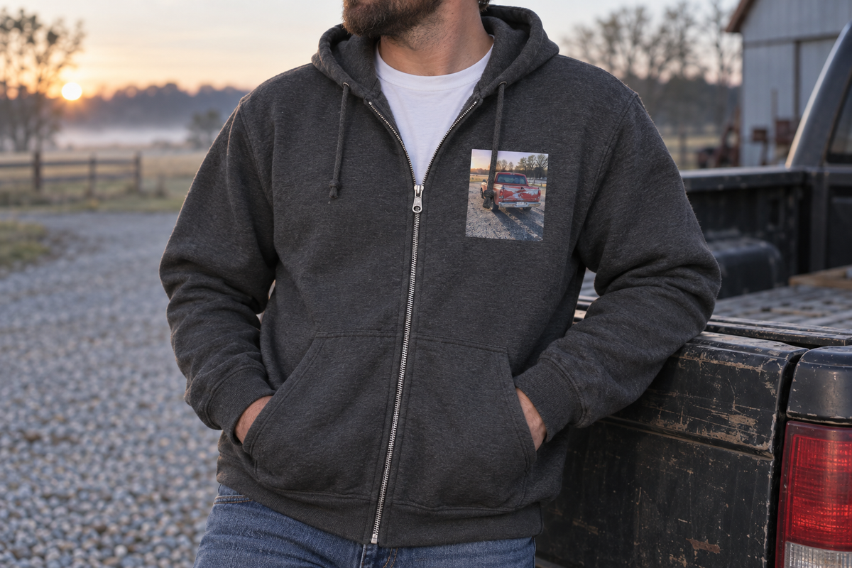 A dark heather custom zip-up hoodie worn open over a tee, metal zipper, drawstring hood, and front pockets visible