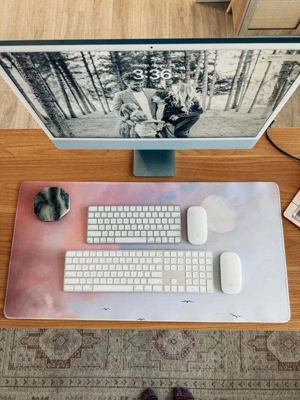 Pink and purple sky photo desk mat under blue iMac on wooden desk